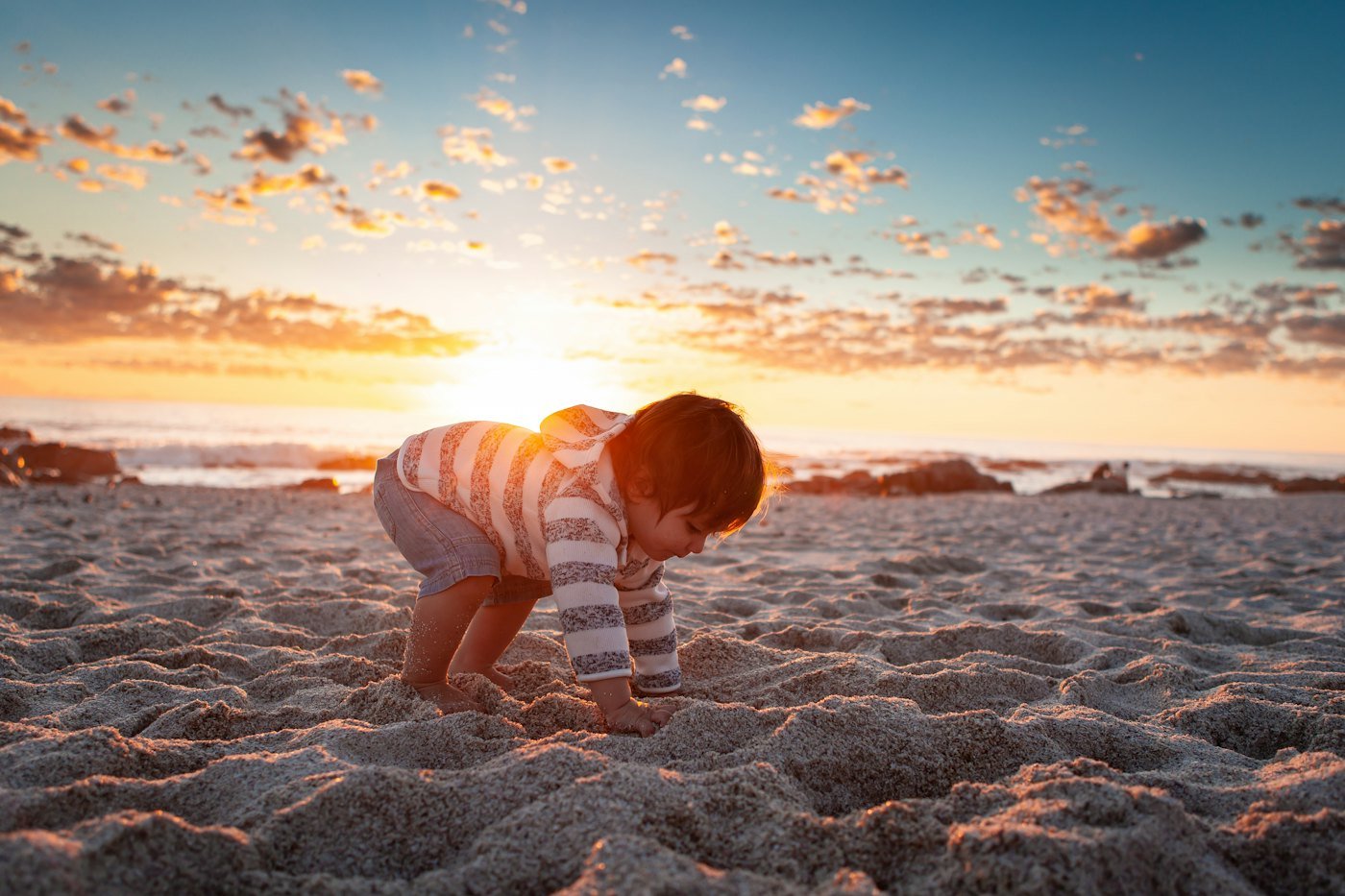A baby crawling on the sand at sunset