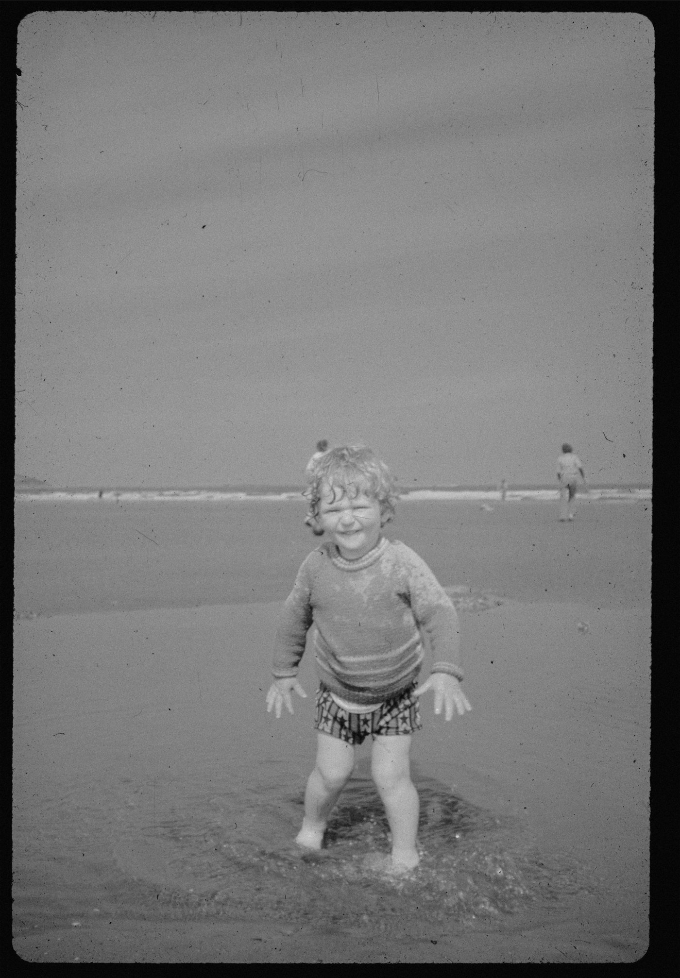 A toddler standing in the shallows, photographed on black and white film