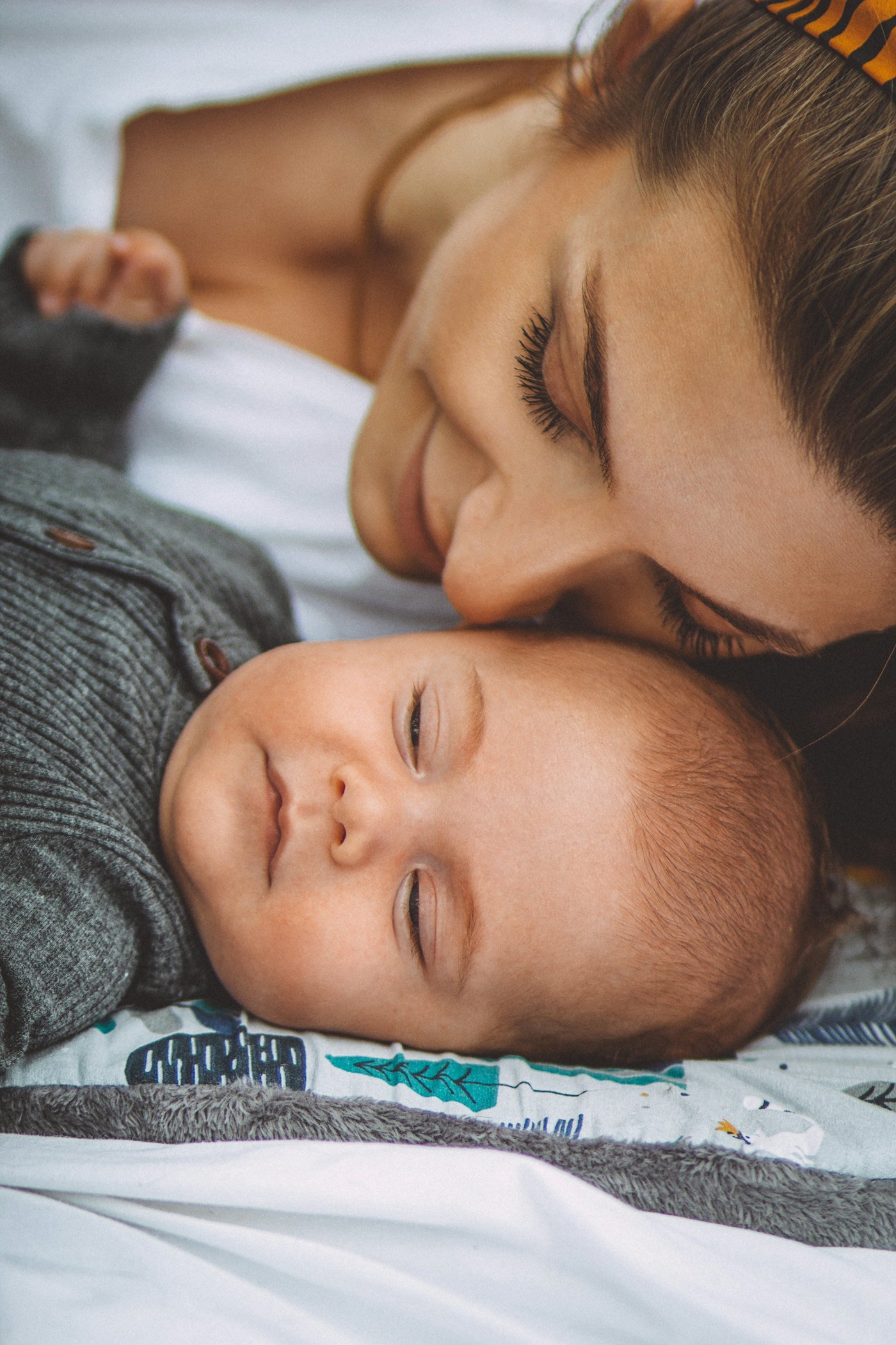 A mother kissing her sleeping baby in bed