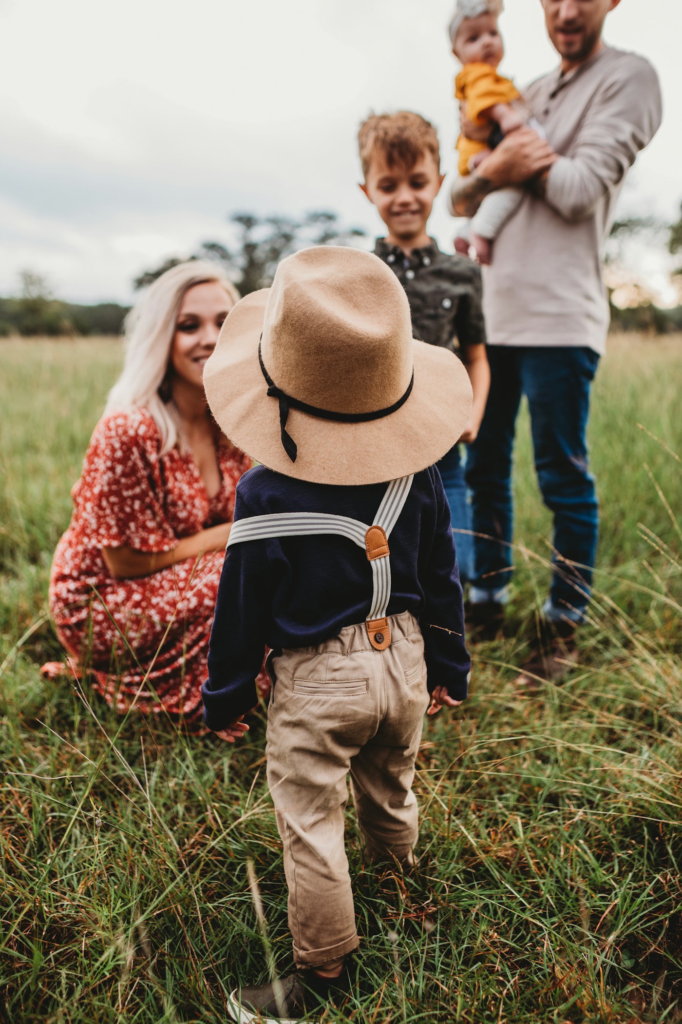 A family laughing together in long grass while a small boy in a sun hat looks on