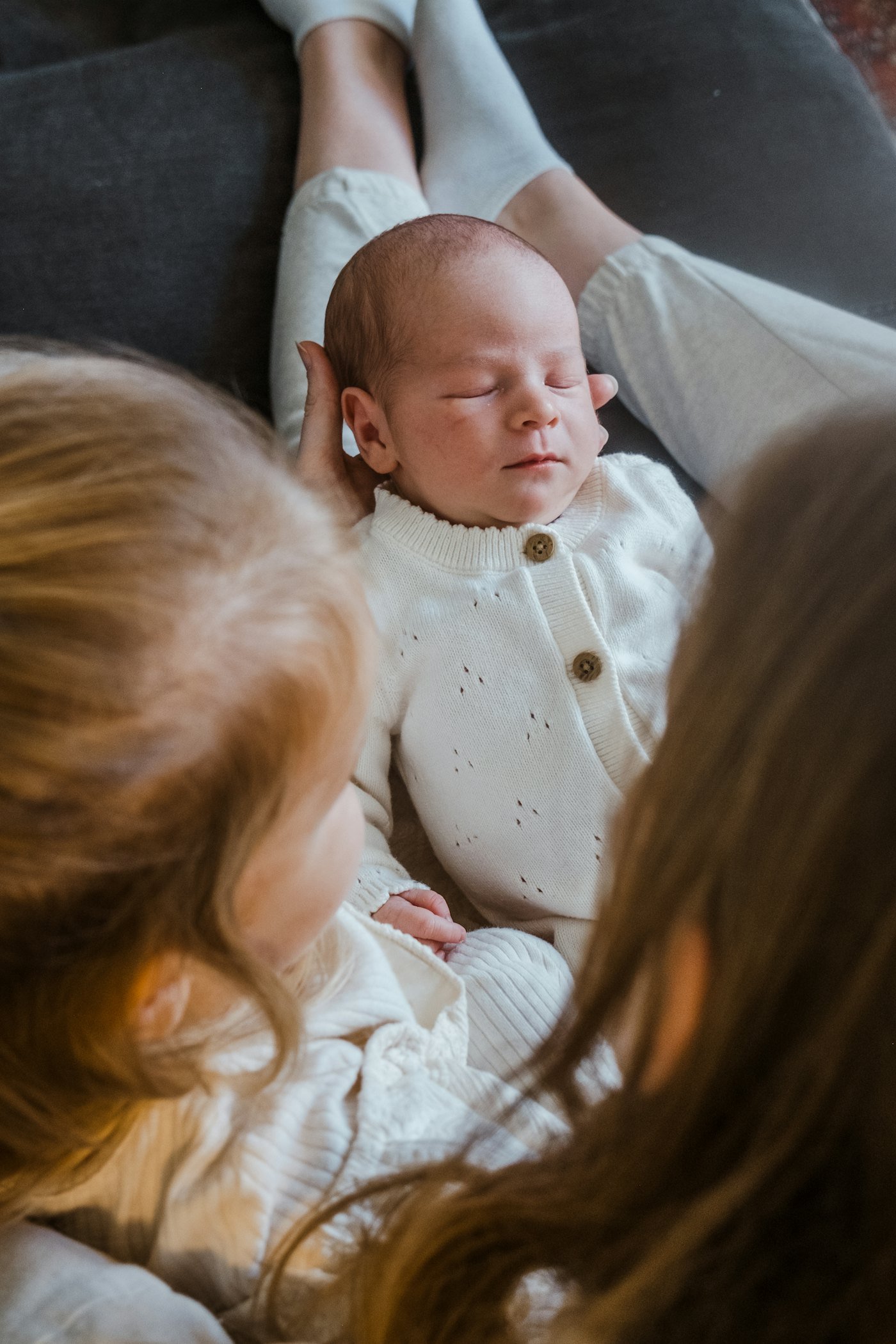 A newborn baby lying between two big sisters