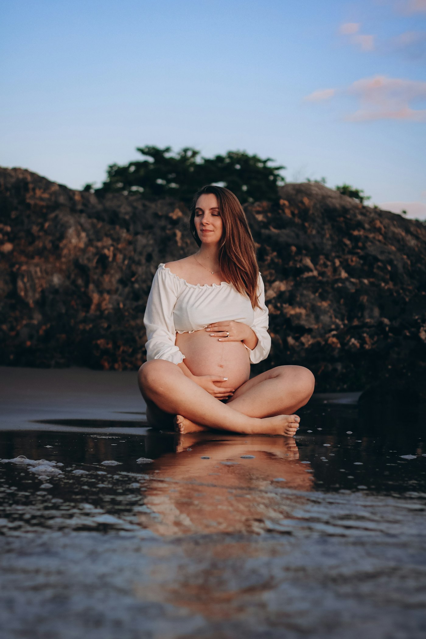 A pregnant woman sitting cross legged in a rock pool